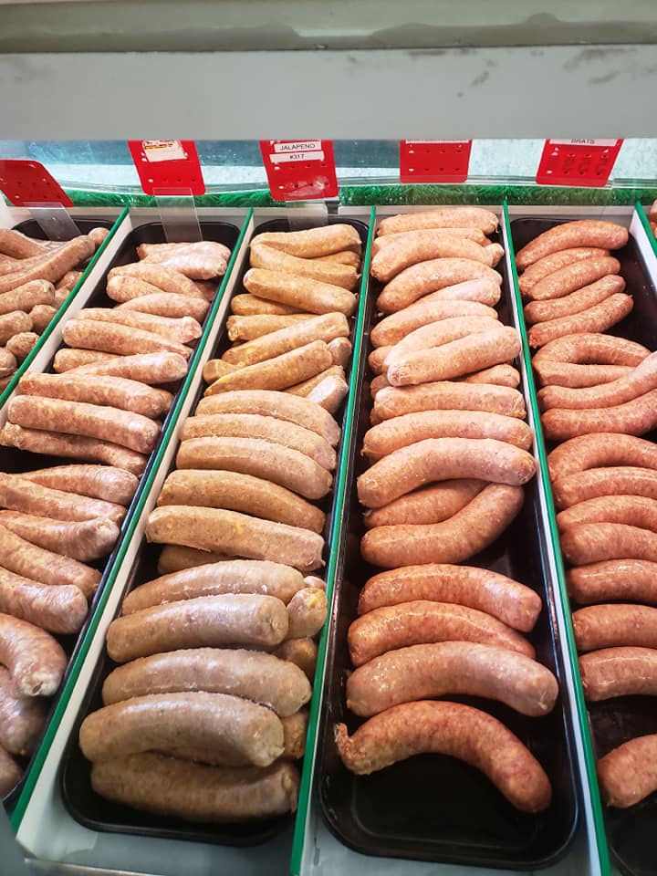 Five varieties of fresh, uncooked sausages and bratwurst displayed in long vertical rows in the Ready Meats store case