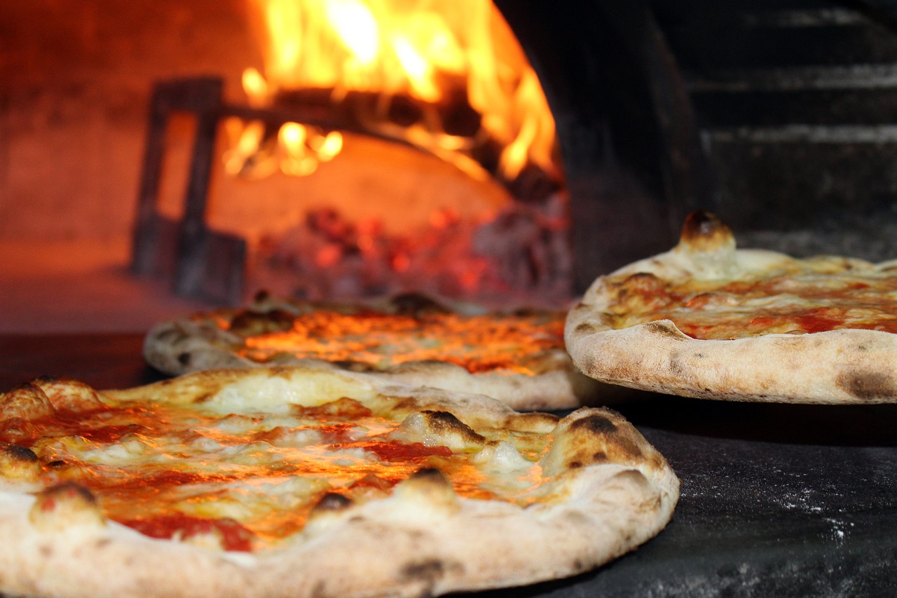 Three tempting pizzas that have been baked with a fiery pizza oven in the background